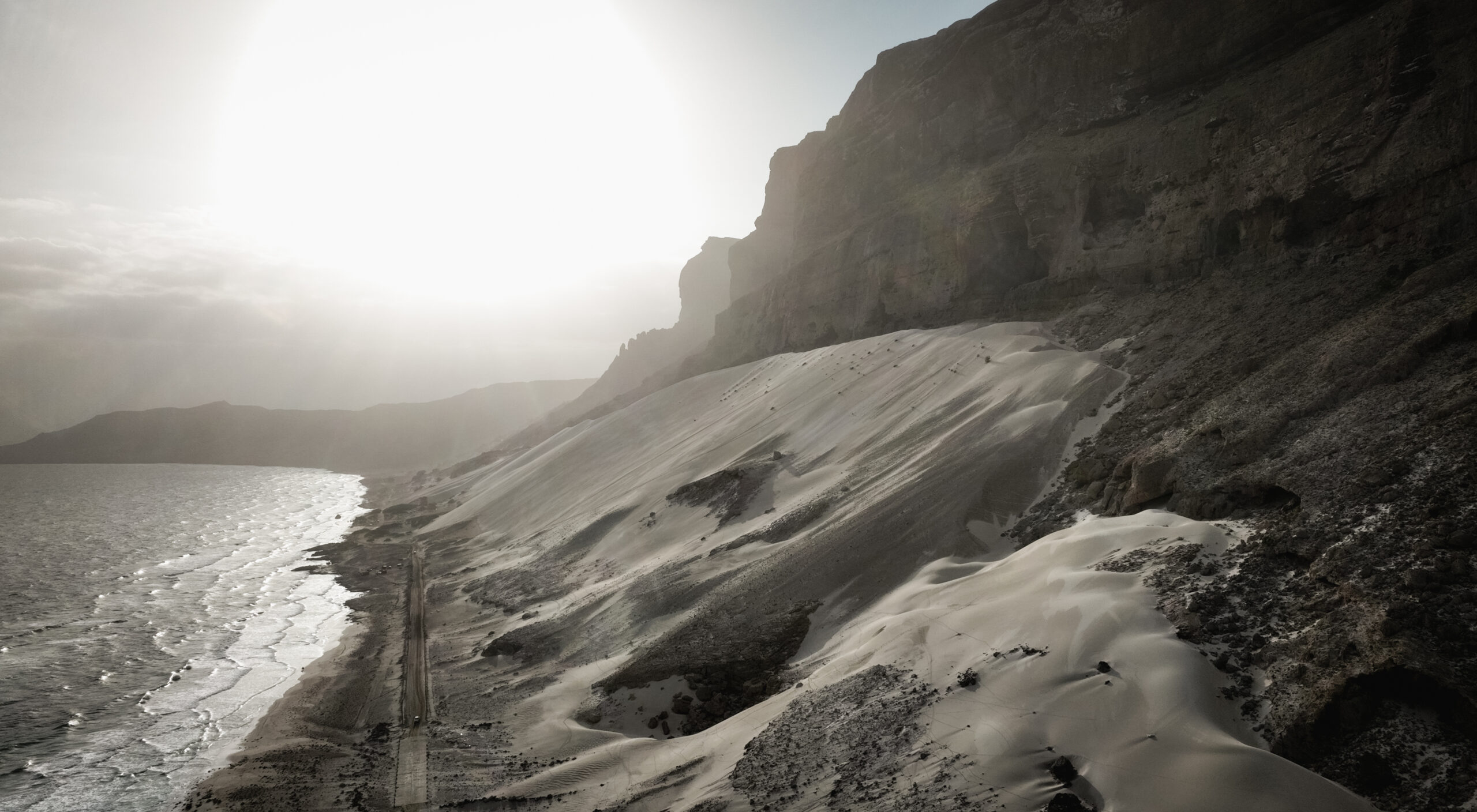 Majestic cliffs above the coastline of Socotra, featuring sandy slopes and a serene ocean at sunset, creating a tranquil atmosphere.