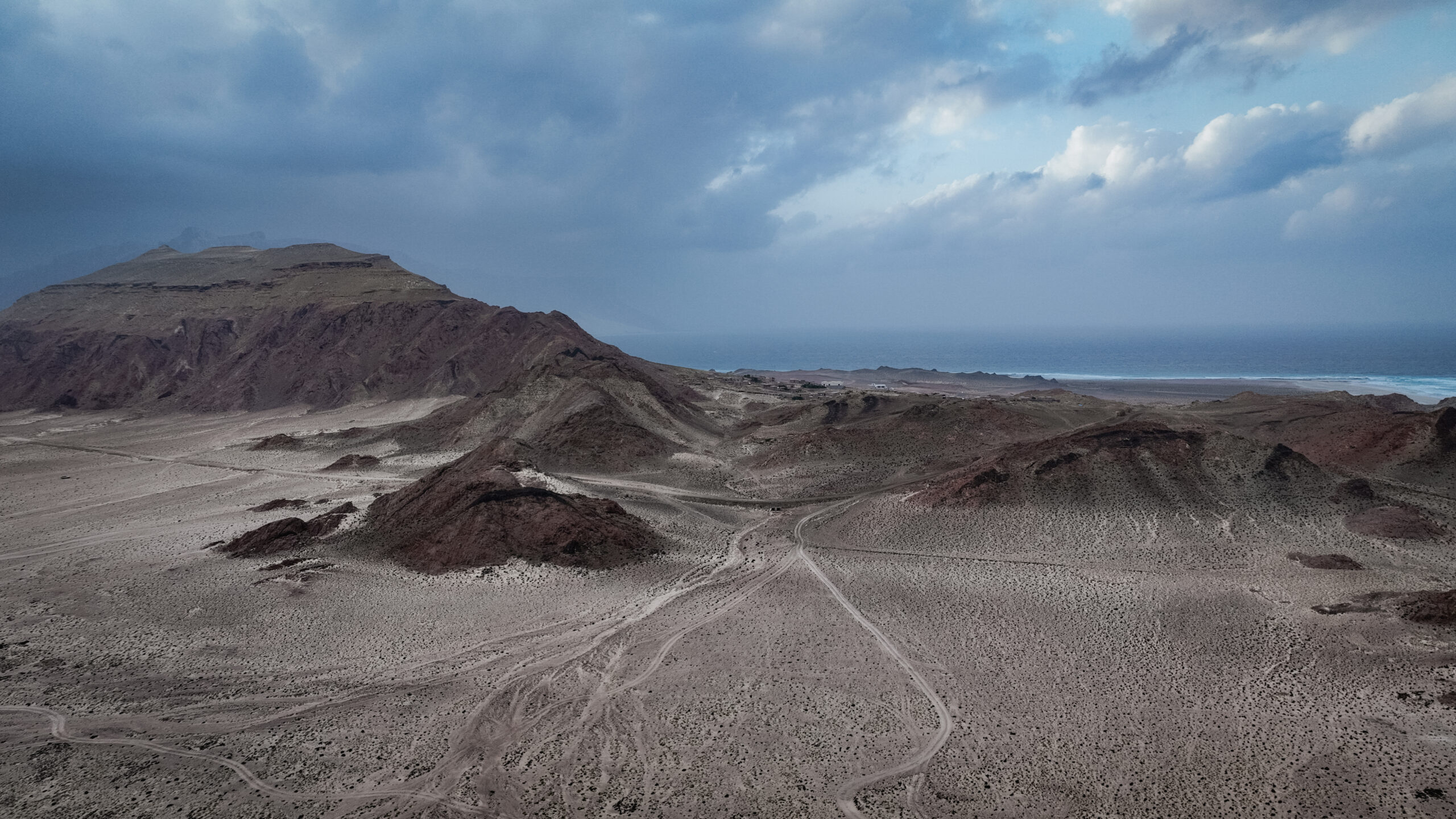 Dramatic terrain stretches across Socotra Island with rugged mountains contrasting against the vibrant coastline under a moody sky.